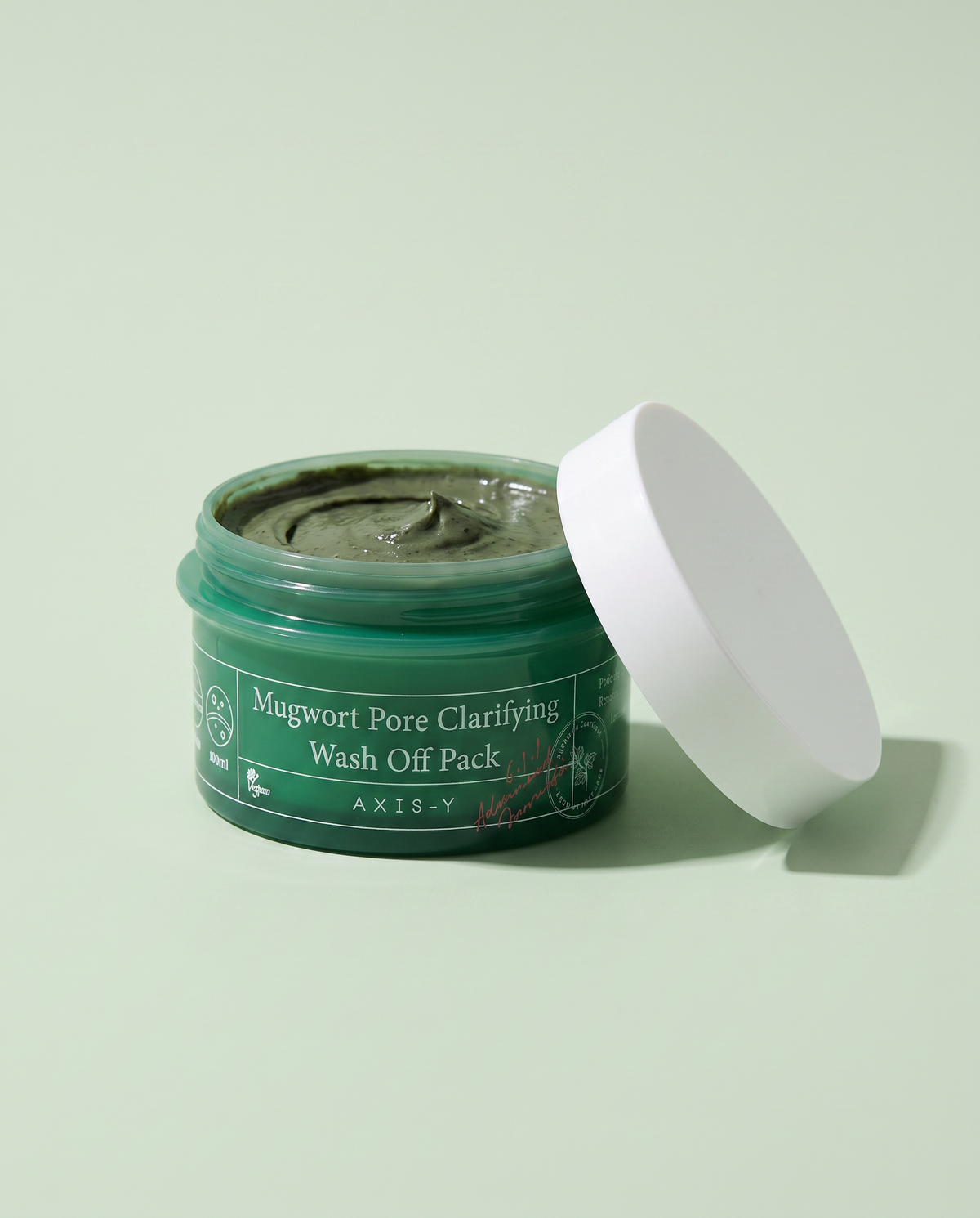 AXIS-Y Mugwort Pore Clarifying Mask 100ml - open green jar with the lid beside it, green background