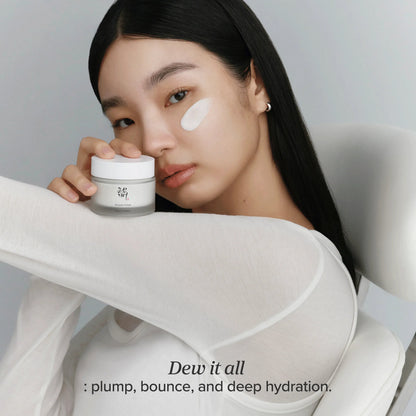 A model holding the Dynasty Cream jar with a swipe of cream on her cheek, tagged dew it all: plump, bounce and deep hydration