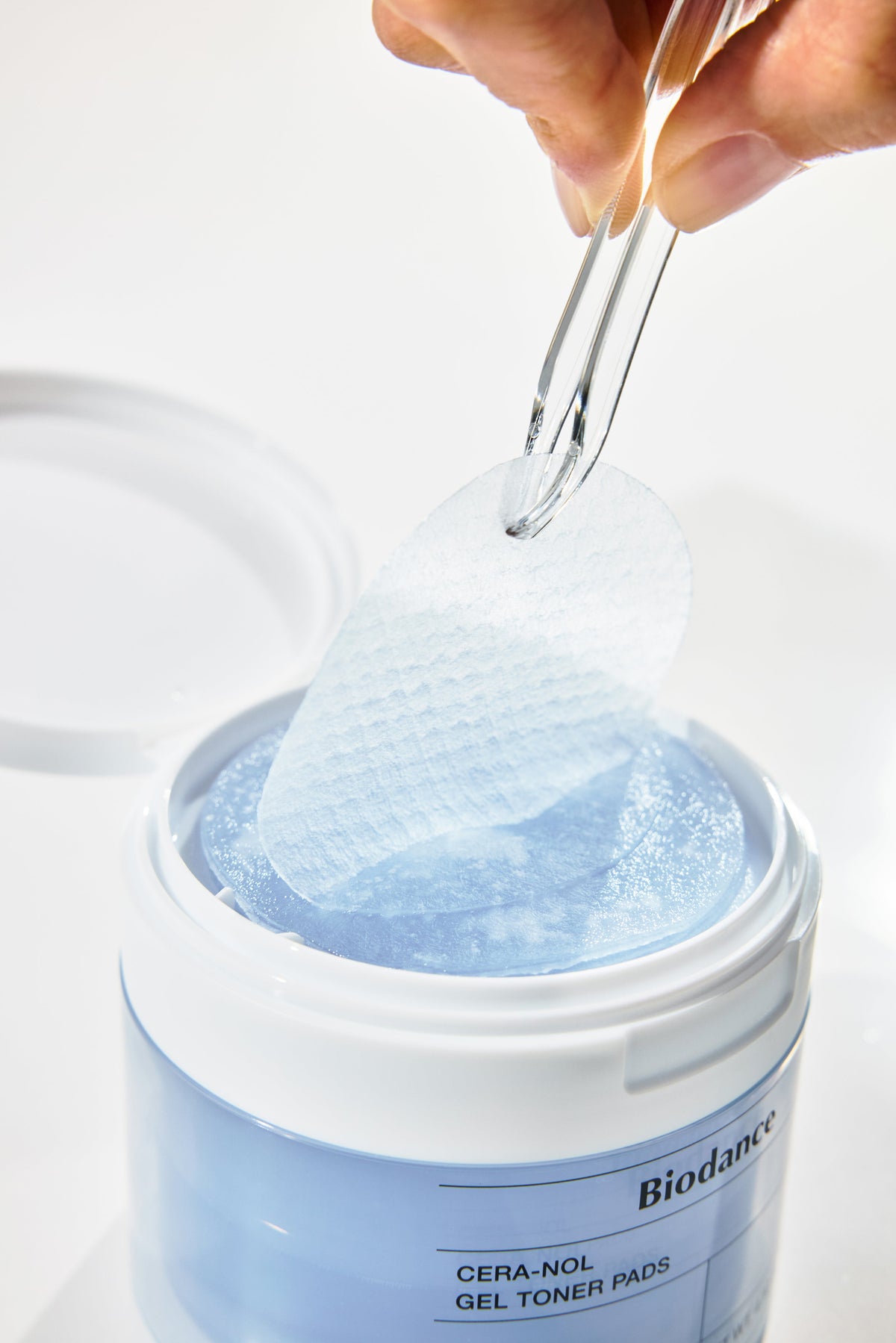 Biodance Cera-NOL Gel Toner Pads 60 Pads 140g - tweezers lifting a gel pad from the open blue jar, blue background
