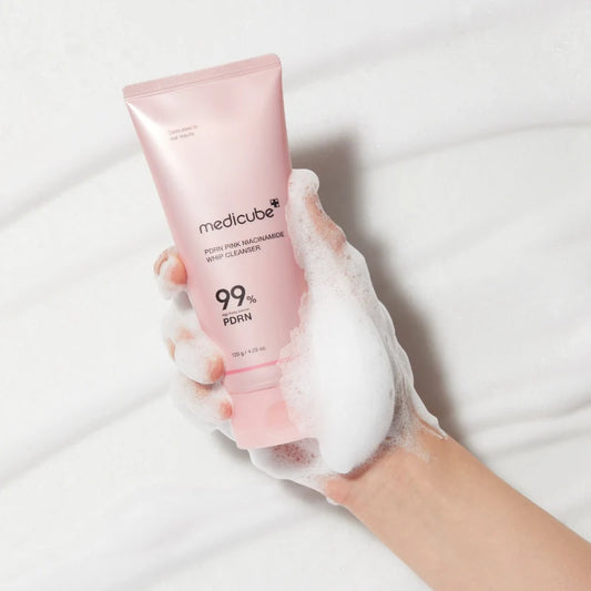 A hand holding the whip cleanser tube covered in thick white foam