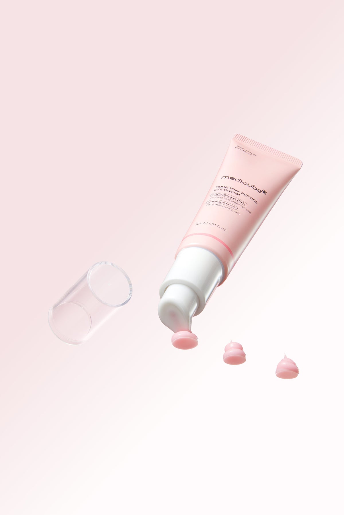 Medicube PDRN Pink Peptide Eye Cream 30ml - pink tube on its side with the cap off and drops beside it