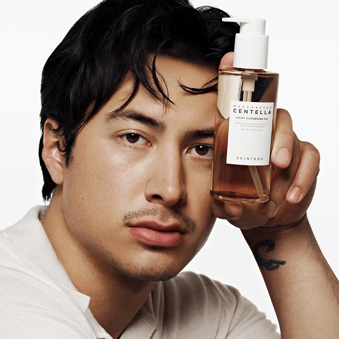 A model holds SKIN1004 Madagascar Centella Light Cleansing Oil 200ml beside his face
